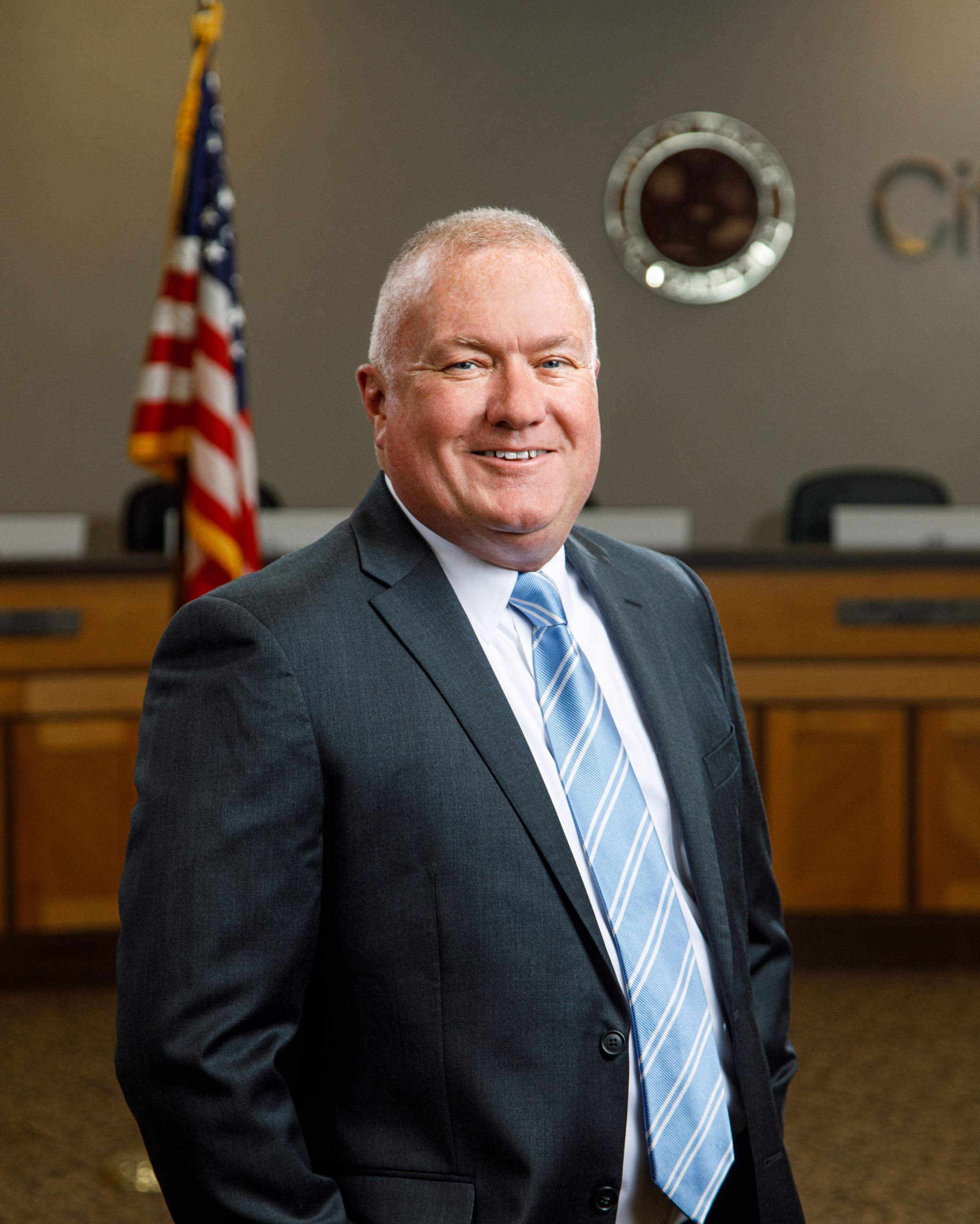 Man posing with American flag over right shoulder in background