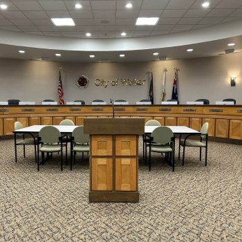 Wooden podium facing wooden pulpit with various local, state, and federal flags in background